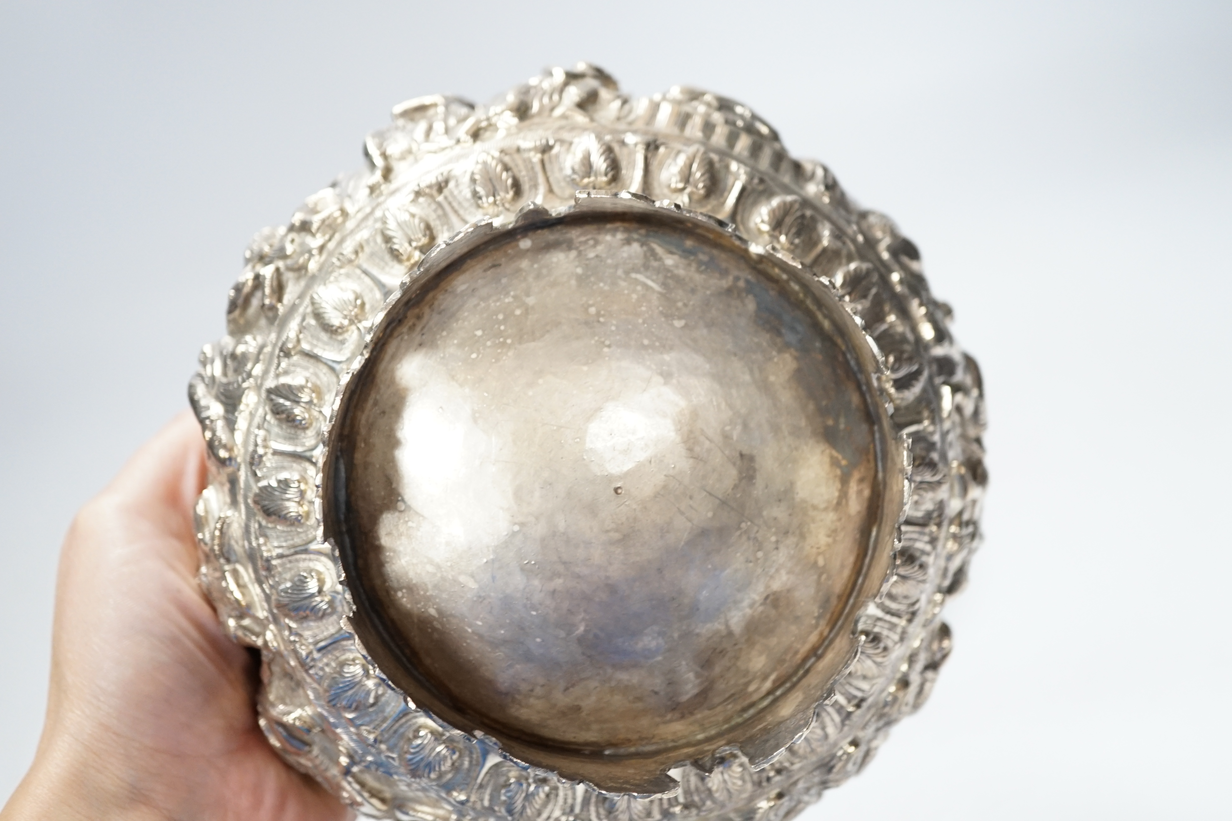 An Indian circular white metal bowl, decorated with a continuous band of figures in a landscape, on scrolled feet with hardwood stand, diameter 16cm